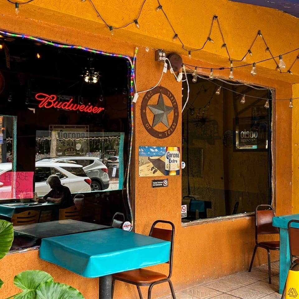 A vibrant yellow and orange restaurant exterior with an "OPEN" sign, outdoor seating, and string lights.