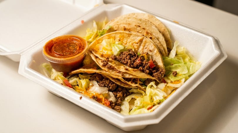 Three soft tacos filled with ground beef, lettuce, and cheese, with a side of salsa.