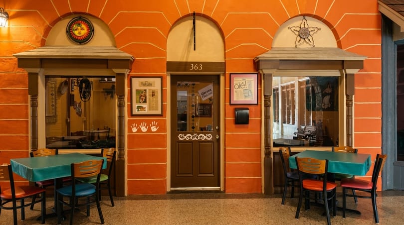 Vibrant orange restaurant facade with a brown door, two windows, and outdoor dining tables.