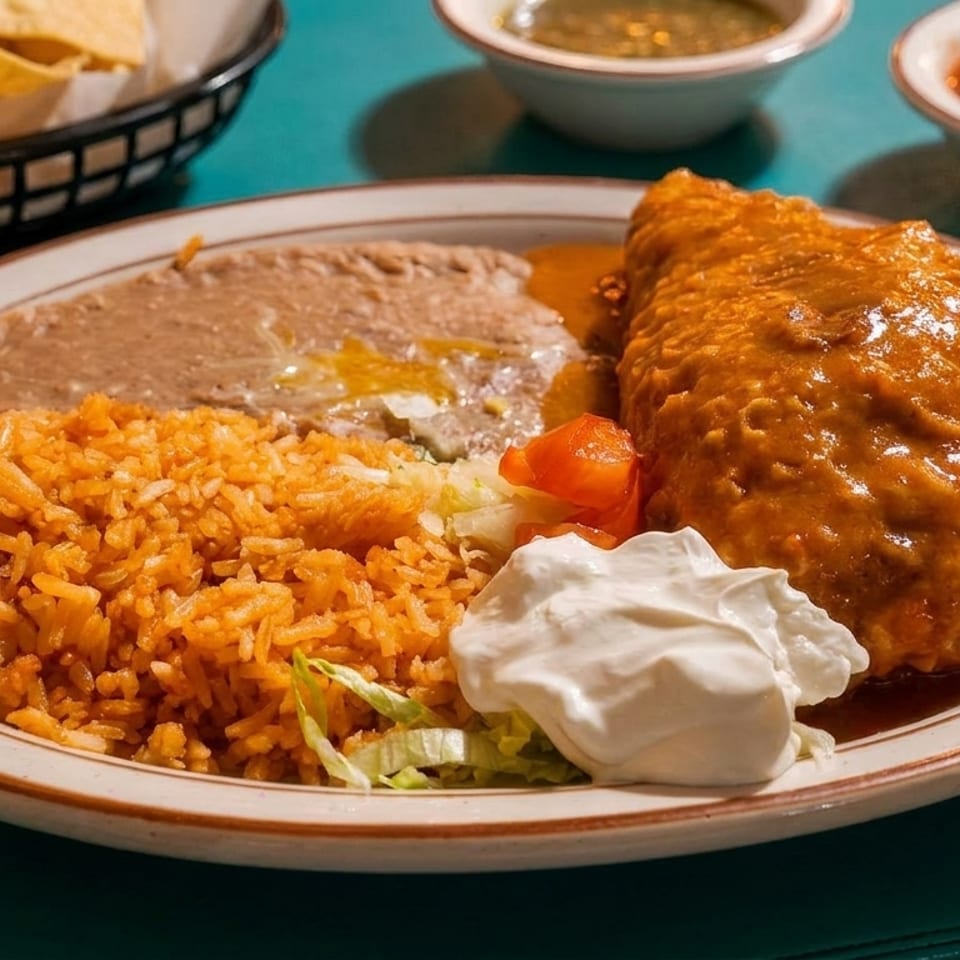 A plate of Mexican food with a chile relleno, rice, refried beans, and sour cream.