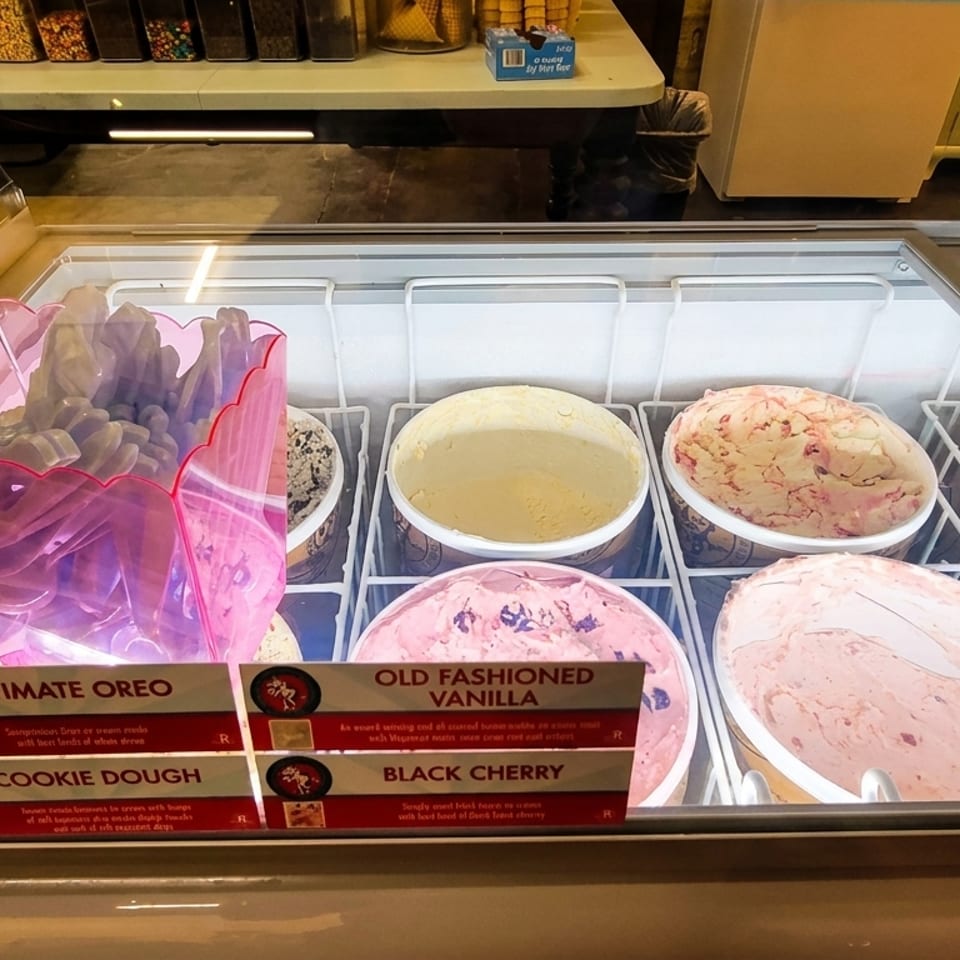 A brightly lit ice cream display case with various flavors and topping options.